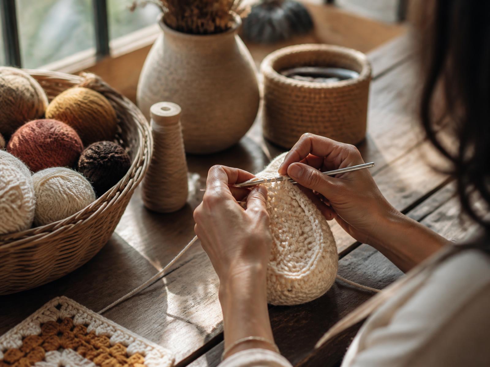 Hands crocheting cream yarn at a sunlit atelier table